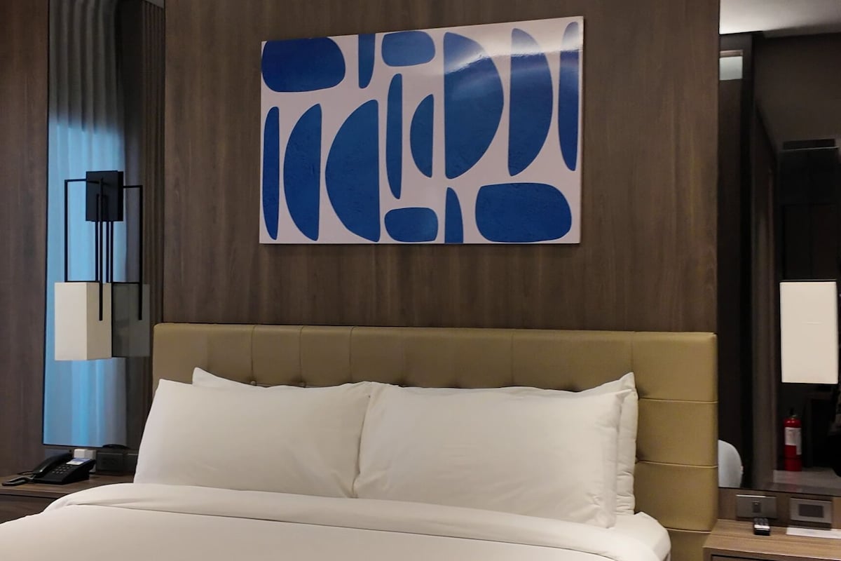 Habitación de hotel con una cama grande, una mesita de noche, una obra de arte colgada en la pared y un espejo.