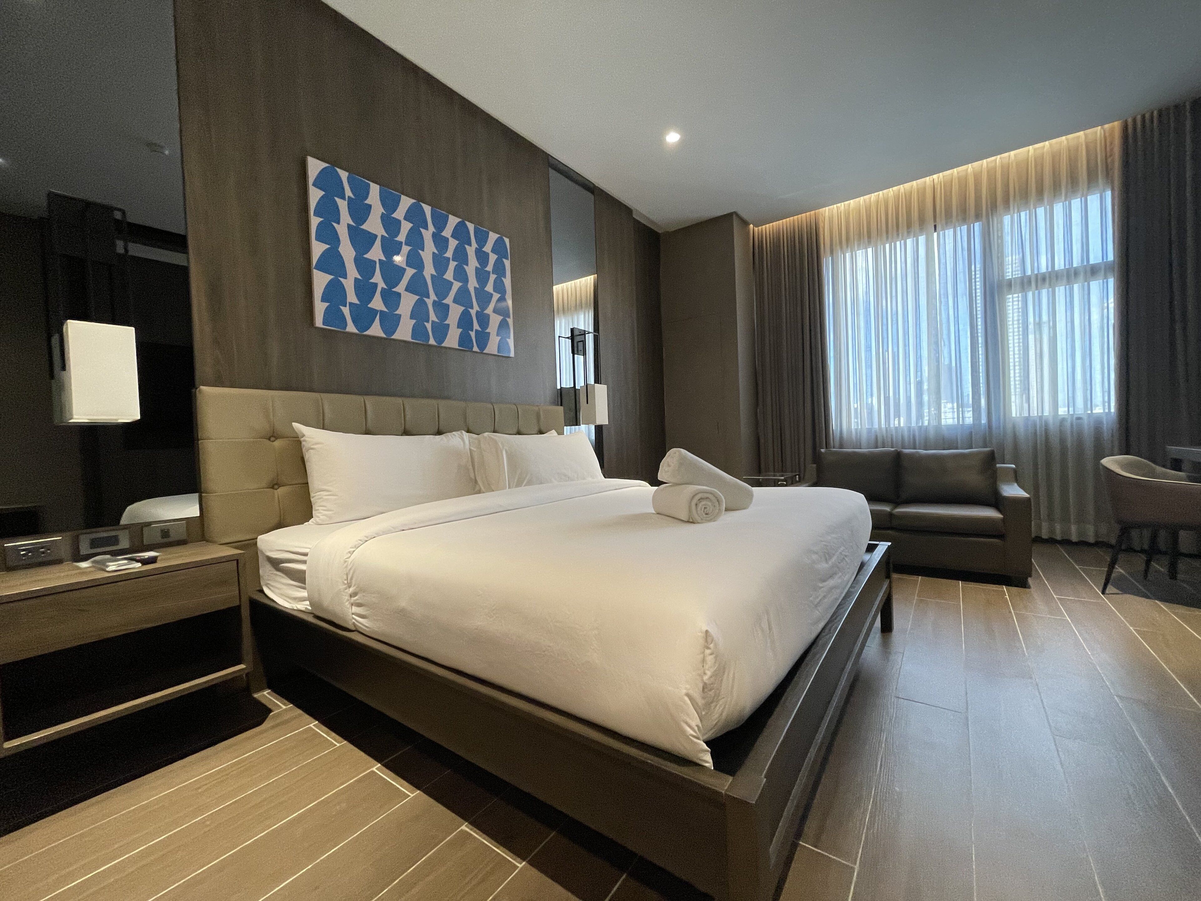 Une chambre d’hôtel moderne dotée d’un grand lit, d’un canapé, d’un bureau et d’une grande fenêtre avec des rideaux.
