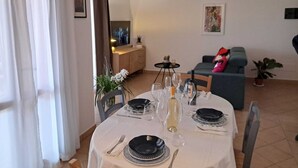 A dining area with a table set for four, a sofa, a TV, and a small table with decorative items. - La Terrazza Del Faro - Stunning 1 bedroom flat 600m from the beach (Pittulongu)