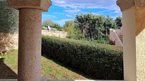 A view through an arched doorway with stone columns, leading to a garden with hedges and trees under a clear sky. - La Terrazza Del Faro - Stunning 1 bedroom flat 600m from the beach (Pittulongu)