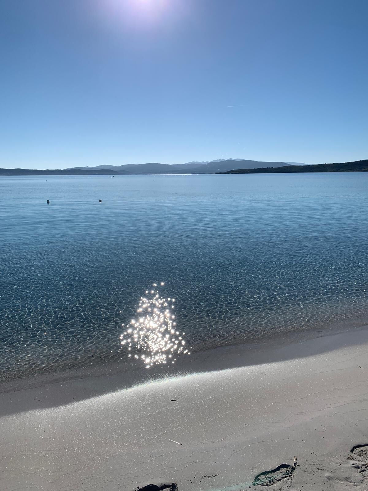 A beach with clear water and distant mountains.