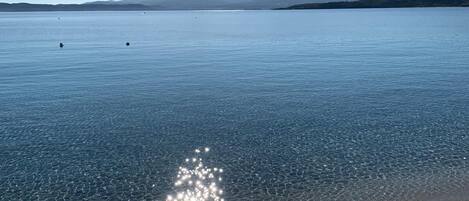 A beach with clear water and distant mountains.