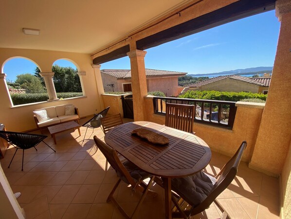 A balcony with a round wooden table, two chairs, a sofa, and a hammock.