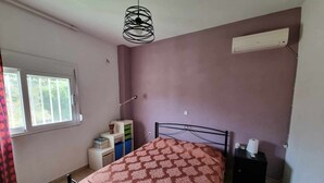 Un dormitorio con cama, mesita de noche, lámpara, ventana y aire acondicionado.