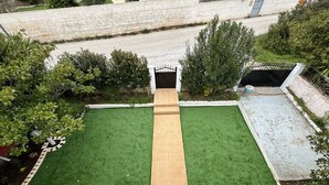 Jardín rectangular con un sendero central, rodeado de diversas plantas y una entrada con reja.