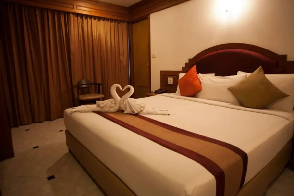 A hotel room with a large bed, a wooden headboard, and a heart-shaped towel arrangement.