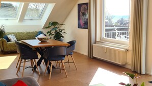 A modern living room with a glass coffee table, a sofa, a dining area with a table and chairs, and a large window with a view.