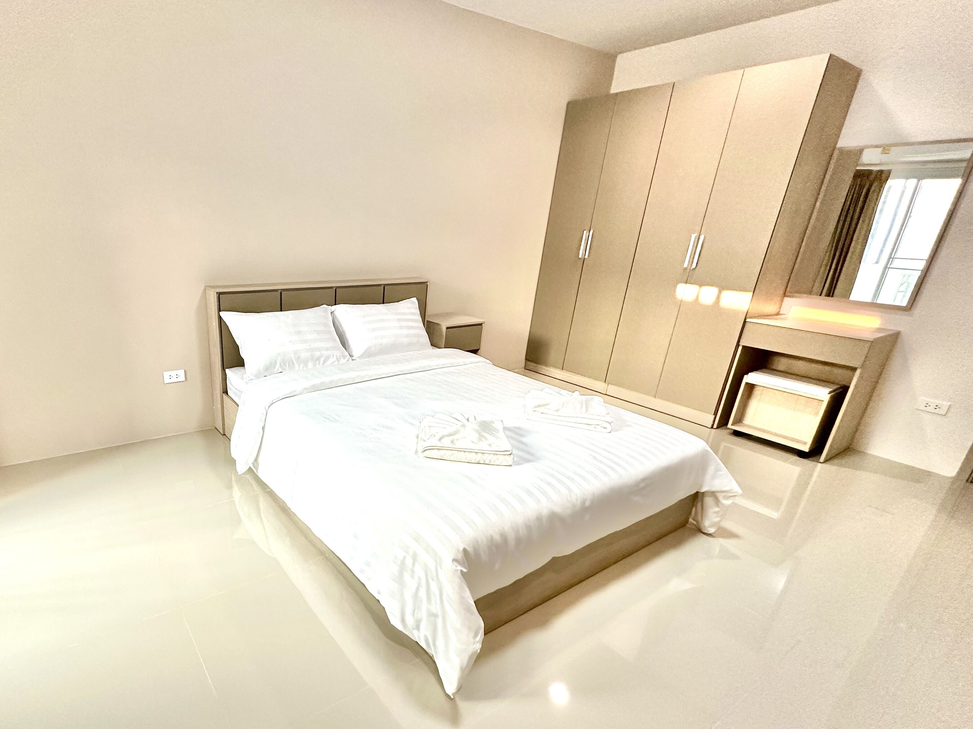 A modern bedroom with a large bed, a wardrobe, and a vanity with a mirror.
