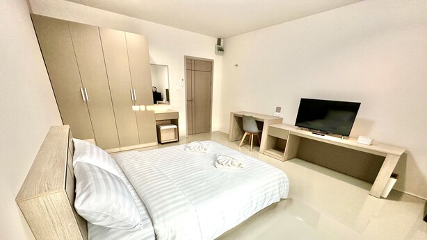 A modern bedroom with a large bed, a TV, a desk, and a wardrobe.