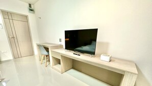 A modern room with a flat-screen TV on a wooden TV stand, a desk, and a chair.