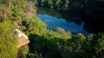 A thatched-roof hut nestled among dense forest, overlooking a calm lake.
