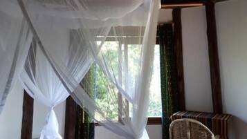 A room with a bed under a canopy, a woven chair, and a thatched ceiling.