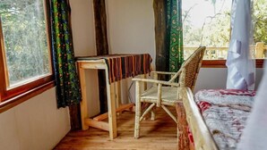 A room with a wooden desk, wicker chair, and a bed with a patterned bedspread. - Lake Nkuruba Nature Reserve (Fort Portal)