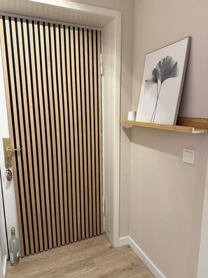 Una stanza con una porta a persiane in legno, un quadro incorniciato su uno scaffale e una bottiglia sul pavimento.