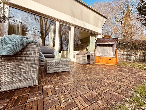 Un patio moderno al aire libre con muebles de mimbre, una caseta pequeña para perros y una casita de juegos de madera.