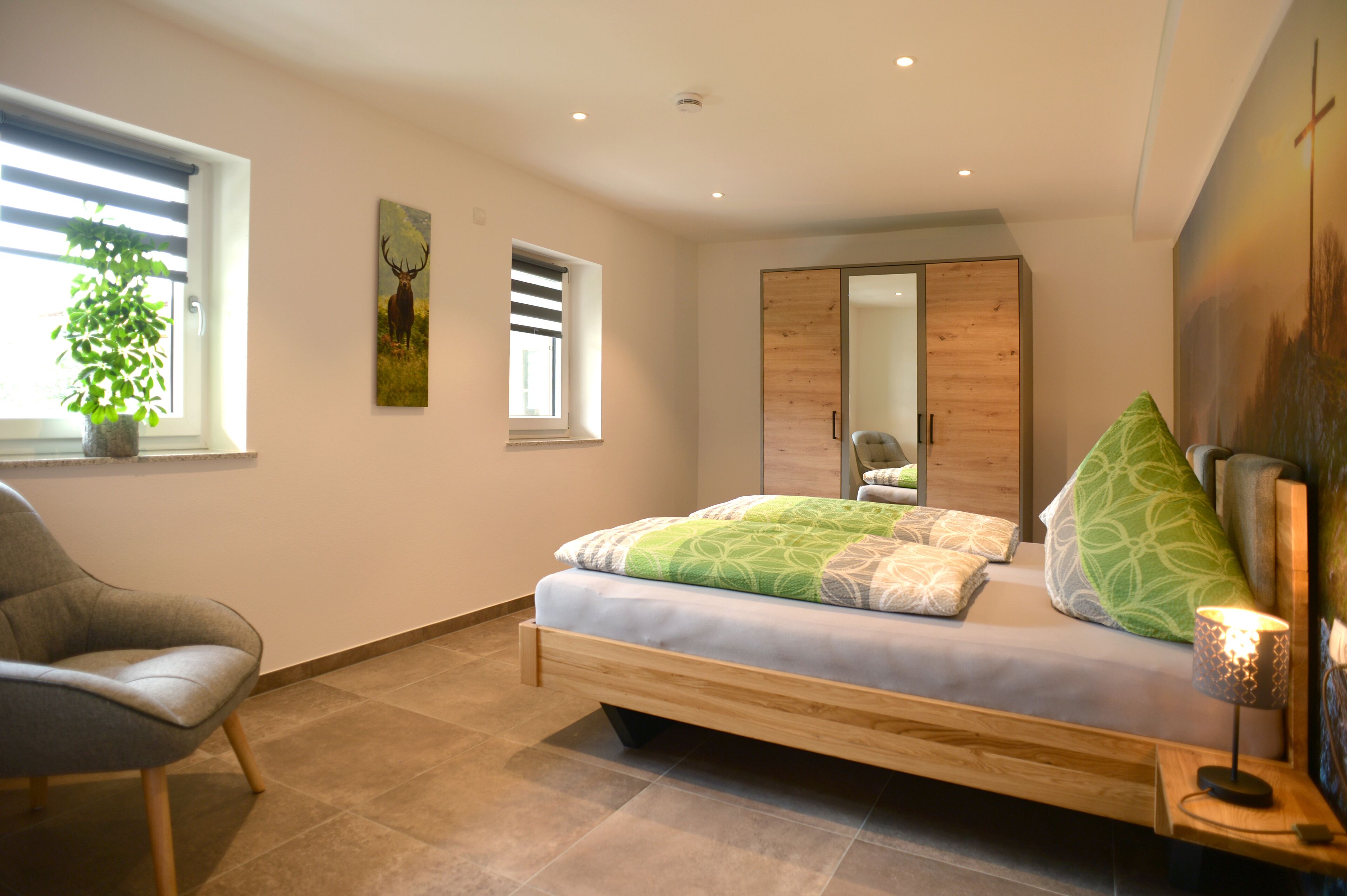 A modern bedroom with a bed, a chair, a plant, and a painting on the wall.