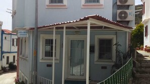 A two-story building with a covered porch and a small garden area. - ArkaDeniz Konukevi Bozcaada (Bozcaada)