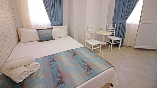 A bedroom with a bed, two white chairs, a small table, and a blue and orange patterned blanket. - ArkaDeniz Konukevi Bozcaada (Bozcaada)