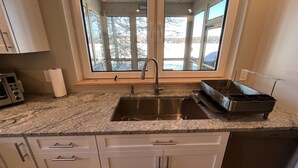 A kitchen with a stainless steel sink, a window with a view of trees, and a microwave. - Newer Construction waterfront house with AC and WiFi in Barnstead (Barnstead)