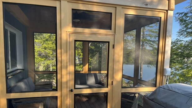A screened-in porch with built-in seating and a table, overlooking a body of water. - Newer Construction waterfront house with AC and WiFi in Barnstead (Barnstead)