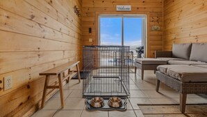 A wooden cabin interior with a pet cage, two pet bowls, a bench, and a sofa. - 5 Min to Lamoine State Park & Lamoine Beach (Lamoine)
