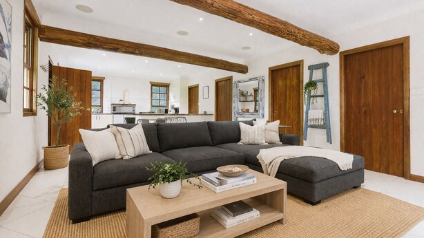 A modern living room with a dark grey sectional sofa, a wooden coffee table, and a kitchen in the background. - South Coast Hinterland Retreat on 30 acres with Rainforest Hikes and Firepit (Broughton Village)