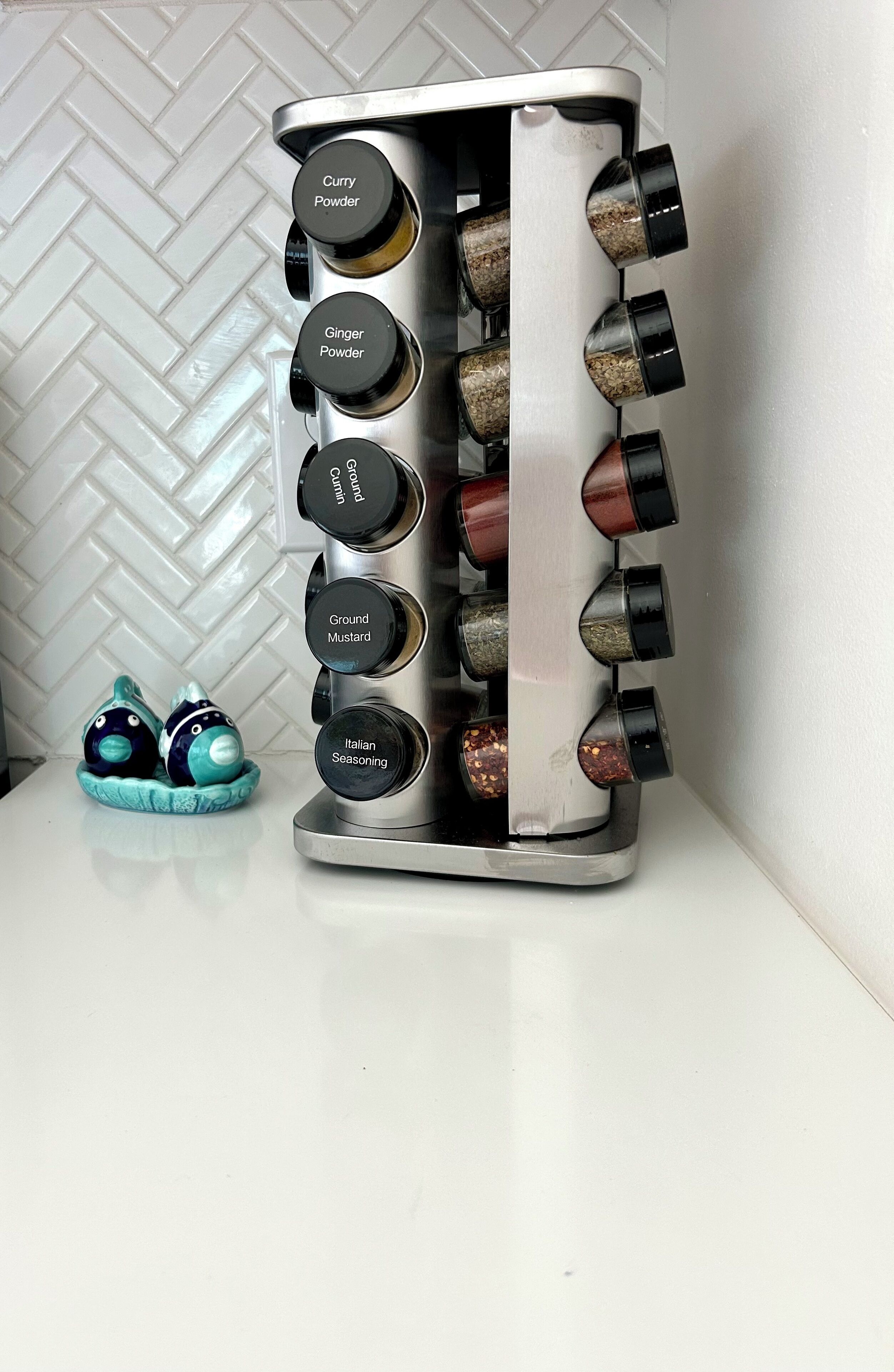 A spice rack with labeled containers for curry powder, ginger powder, ground cumin, ground mustard, and Italian seasoning.
