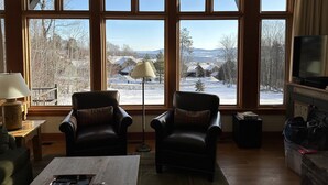 A living room with large windows, two leather chairs, a coffee table, a lamp, and a television.