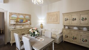 A dining area with a wooden table, white chairs, a chandelier, and a cabinet with fruit designs. - Charme & Chic Studio (Salerno)