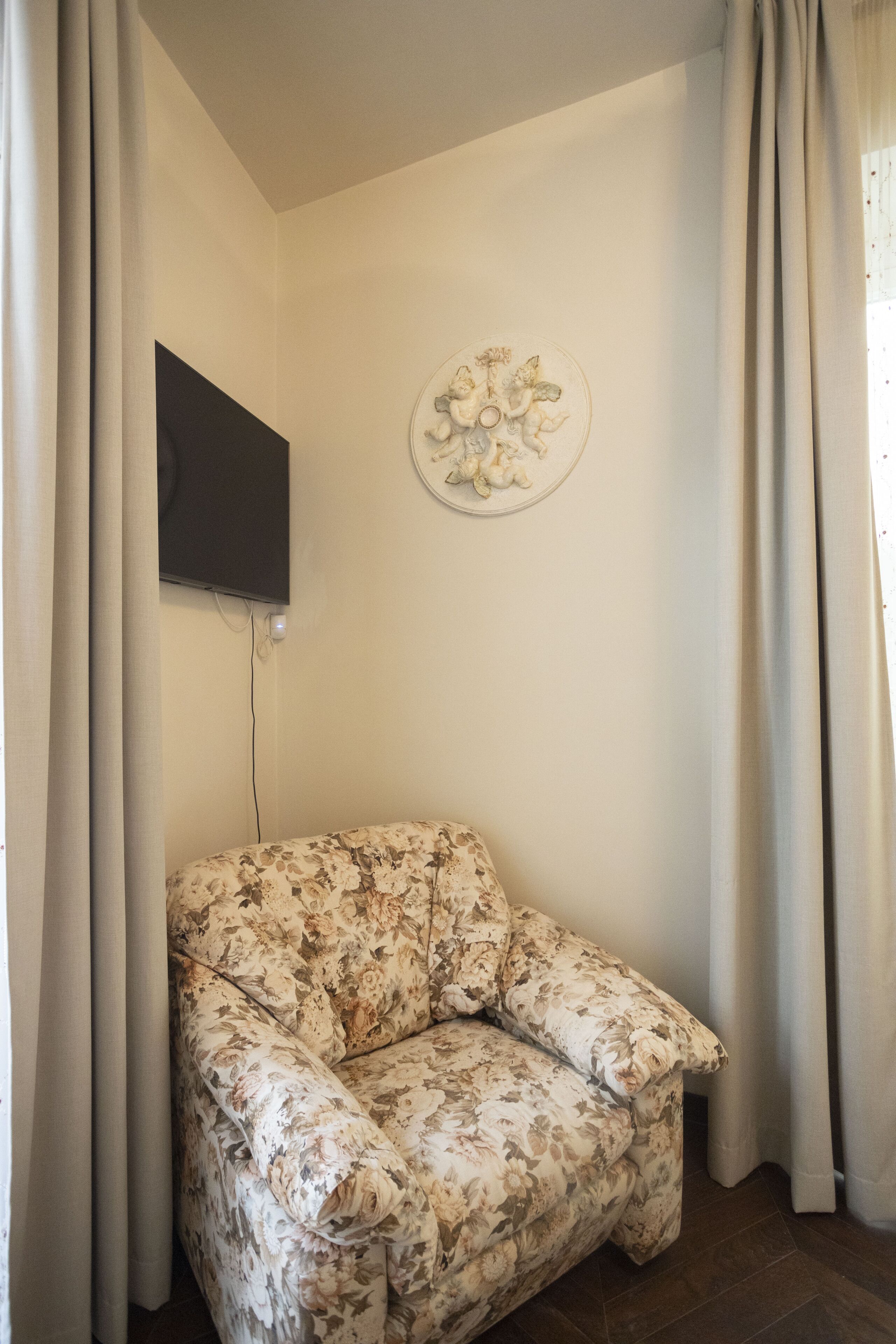 A living room with a floral sofa, a flat-screen TV mounted on the wall, and a decorative plate above it.