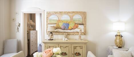 A room with a white sofa, a dining table with a vase of flowers, a cream-colored cabinet, and a wall-mounted painting.