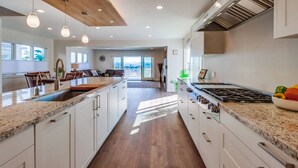 A modern kitchen with a central island, white cabinetry, and a large window providing natural light.