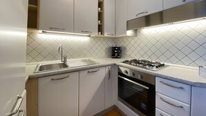 Une cuisine compacte avec des meubles blancs, une hotte en acier inoxydable, une cuisinière à gaz et un four encastré.