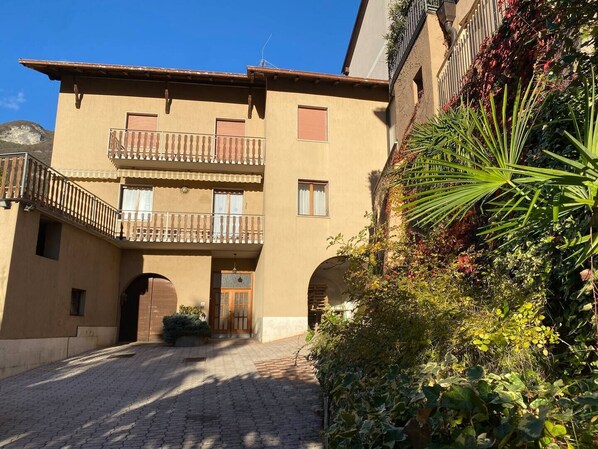 A building with a central entrance, two balconies, and a cobblestone courtyard.
