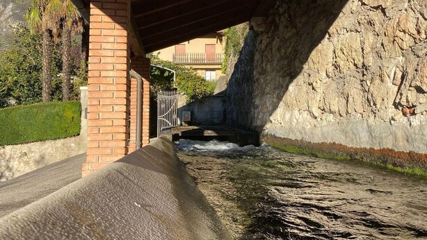Un canal d’eau sous un pont, avec un mur en briques et une grille métallique.