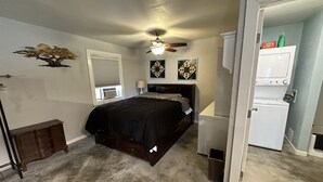 A bedroom with a bed, a ceiling fan, a window with blinds, a dresser, and a laundry area with a washing machine. - Cozy studio cottage in enchanting Lake Charles with AC, WiFi.   (Lake Charles)