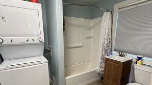 A compact bathroom with a white toilet, a shower with a curtain, a small sink, and a refrigerator. - Cozy studio cottage in enchanting Lake Charles with AC, WiFi.   (Lake Charles)