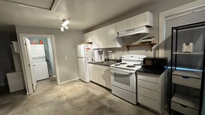 A compact kitchen with white cabinets, a stove, a microwave, and a refrigerator. - Cozy studio cottage in enchanting Lake Charles with AC, WiFi.   (Lake Charles)