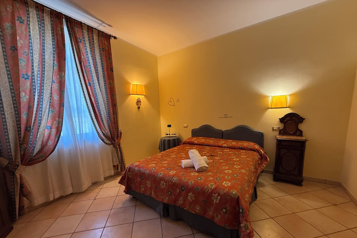 Une chambre d’hôtel avec un lit, deux lampes murales, une horloge et une fenêtre avec des rideaux.