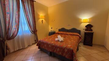A hotel room with a bed, two wall lamps, a clock, and a window with curtains.