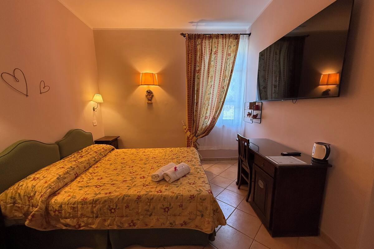 Une chambre d’hôtel avec un lit, des lampes de chevet, un bureau, un miroir et une fenêtre avec des rideaux.