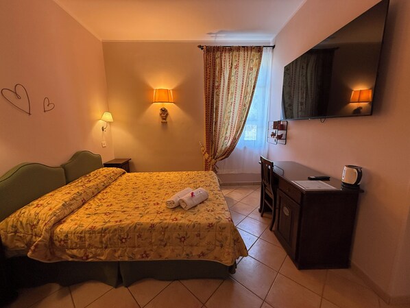Una habitación de hotel con cama, lámparas de noche, escritorio, espejo y ventana con cortinas.