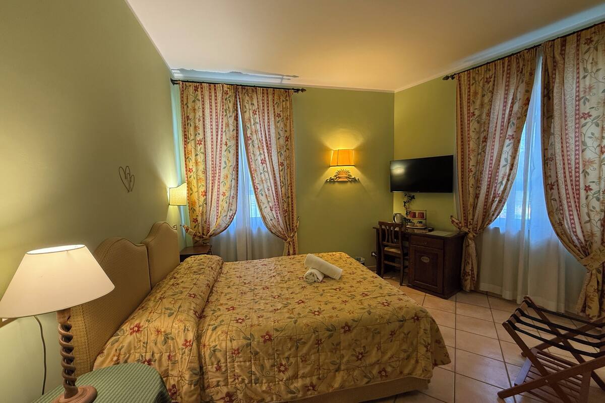 Une chambre d’hôtel avec un lit, un bureau, une chaise, une télévision et des rideaux.