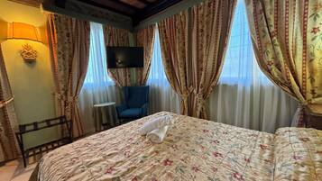 Un dormitorio con cama, una silla, un televisor y cortinas.