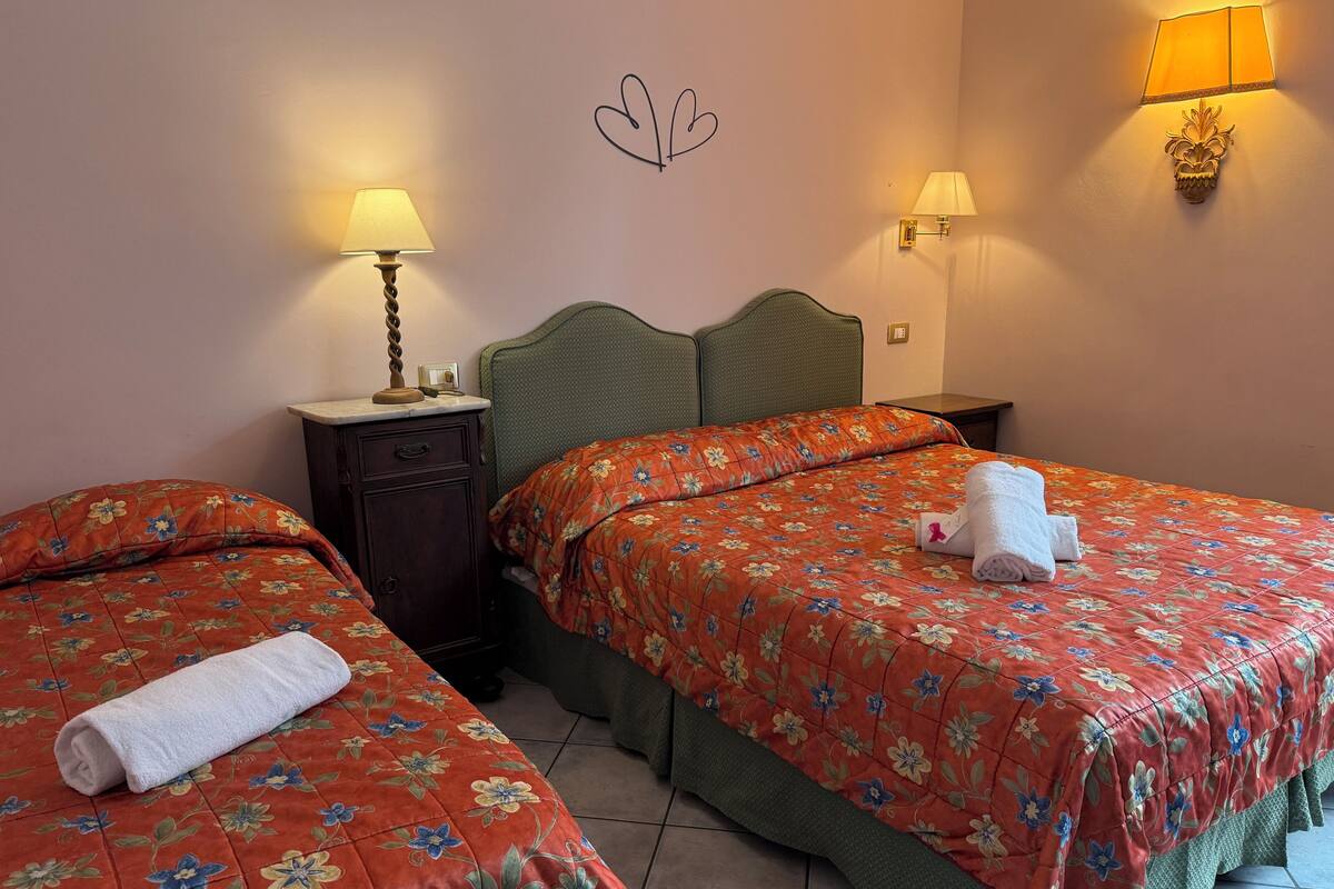 Une chambre d’hôtel avec deux lits, une table de chevet, une lampe et un luminaire fixé au mur.