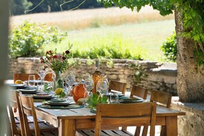 An outdoor dining table set with plates, glasses, and a vase with flowers.