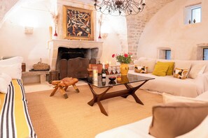A cozy living room with a fireplace, a glass coffee table, and a sofa with cushions.
