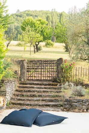 A stone staircase leading to a gated entrance with a view of a green field and trees in the background.