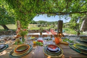 An outdoor dining area with a table set for a meal, surrounded by greenery and a view of the countryside. - Beautiful Bastide in Provence with swimming pool, tennis court, and jacuzzi (CERESTE EN LUBERON)