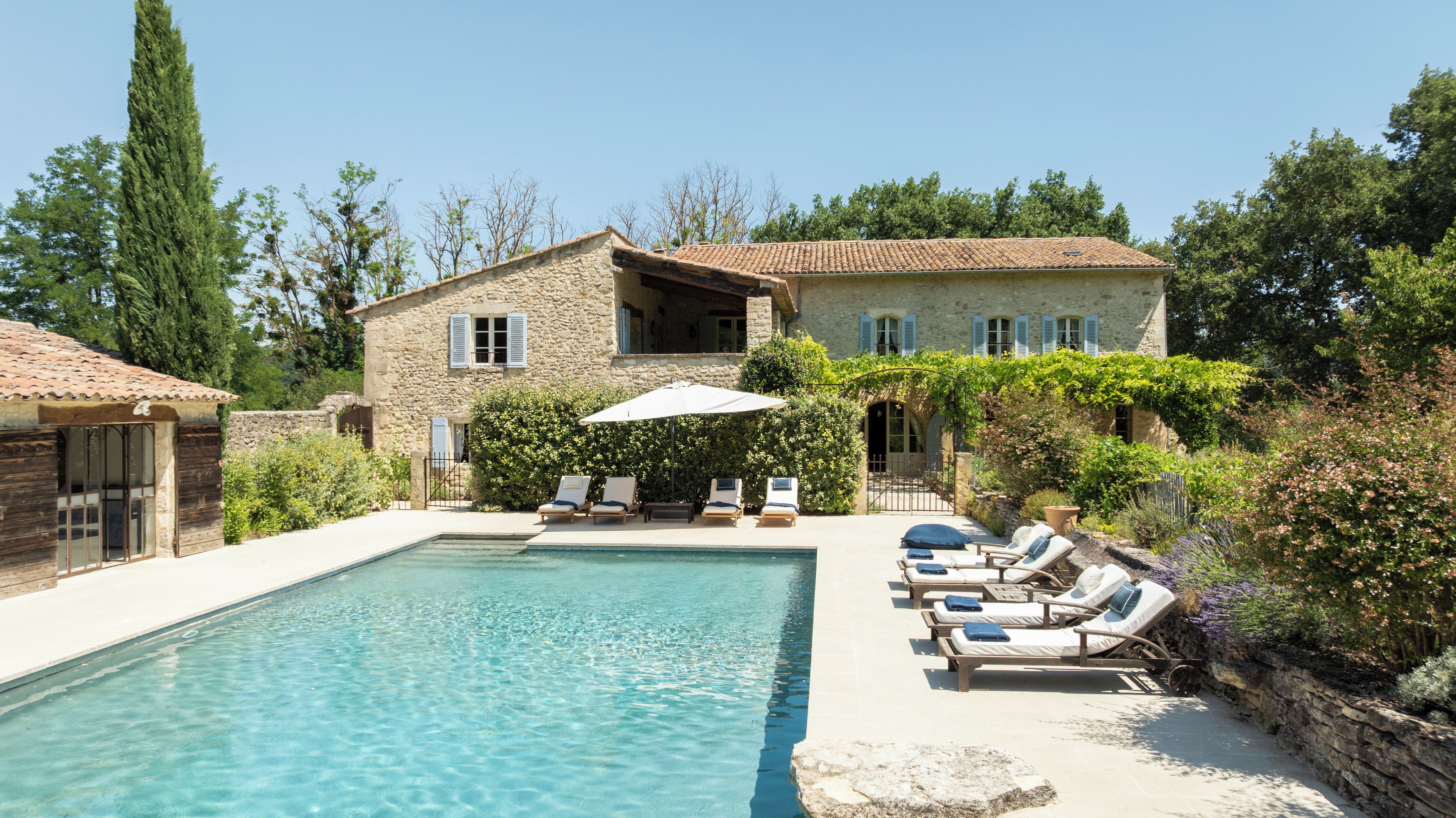 A stone villa with a swimming pool, lounge chairs, and a garden.